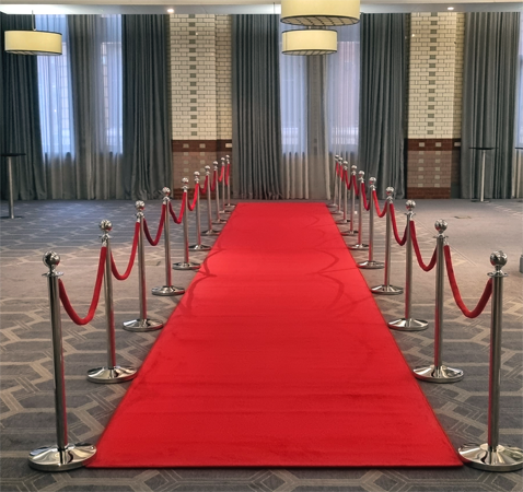 A 14m long deep pile luxury red carpet with polished chrome poles and red velvet ropes within a hotel function suite.